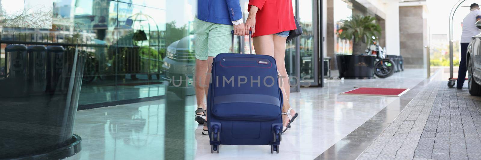 Portrait of couple dressed in luxury suits come to hotel with suitcase. Man and woman arrived on holiday, all inclusive. Trip, vacation, resort concept