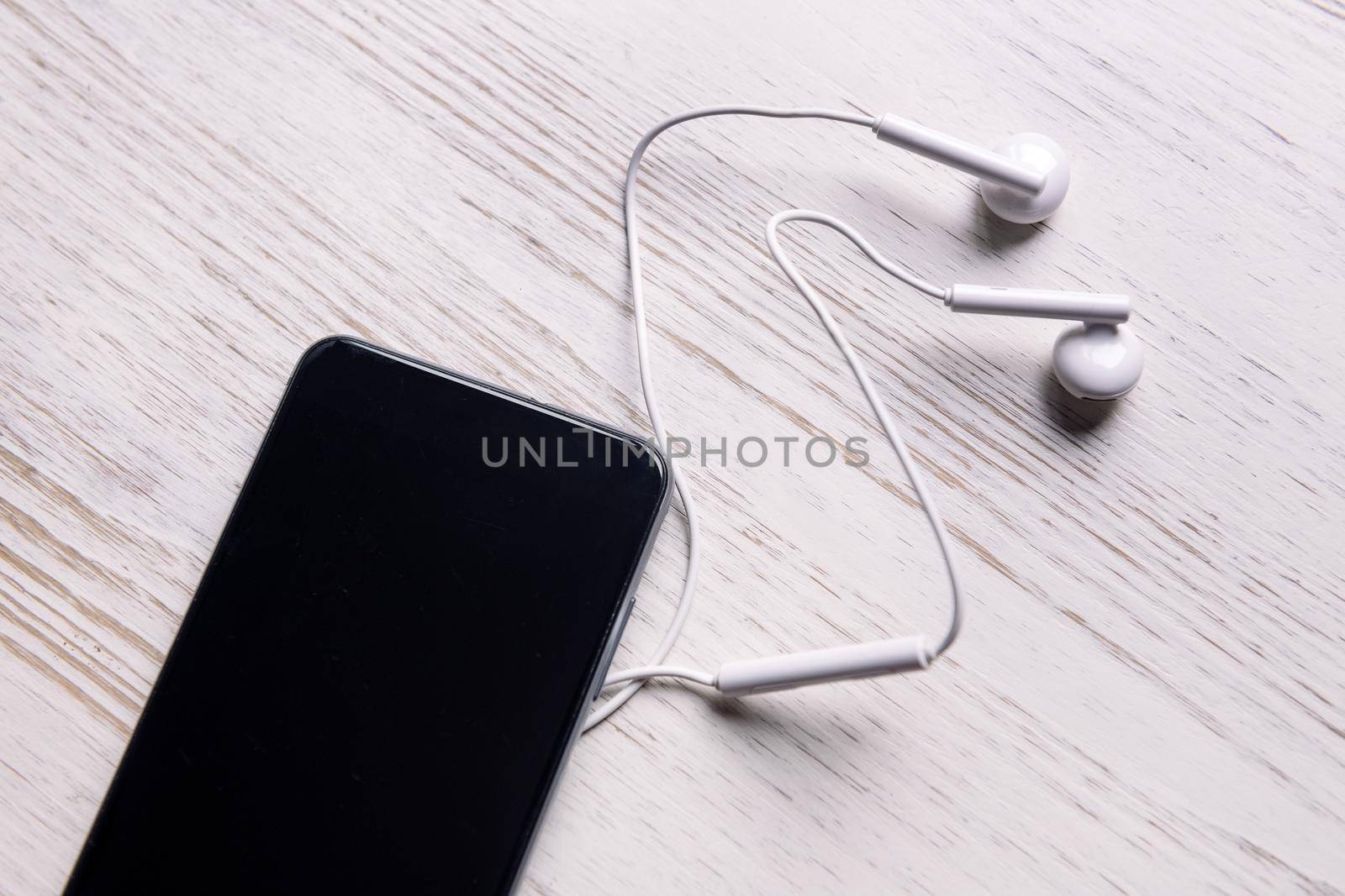 top view of a smart phone with earphones on white wooden table, music and podcast concept, copy space for text