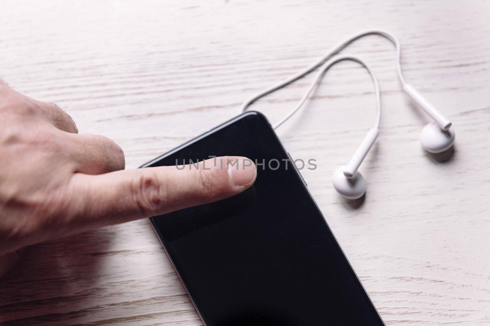 top view of a finger touching a smartphone with earphones on white wooden surface, music and podcast concept, copy space for text