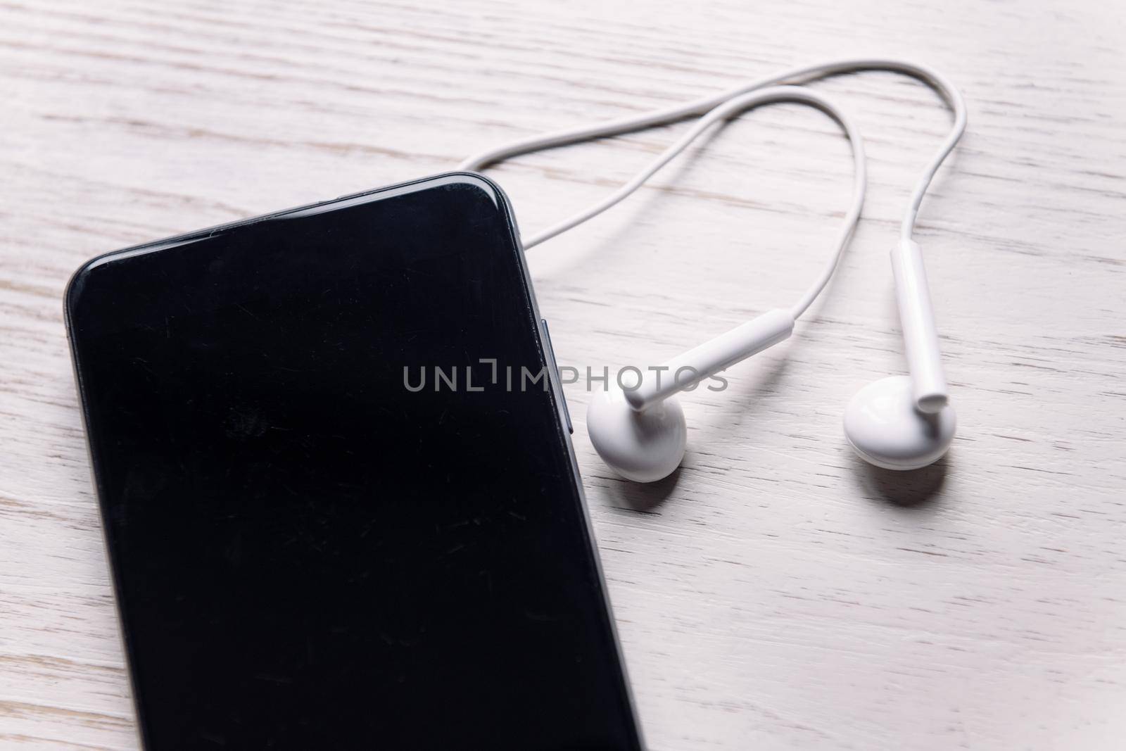 top view of a smartphone with earphones on white wooden surface, music and podcast concept, copy space for text