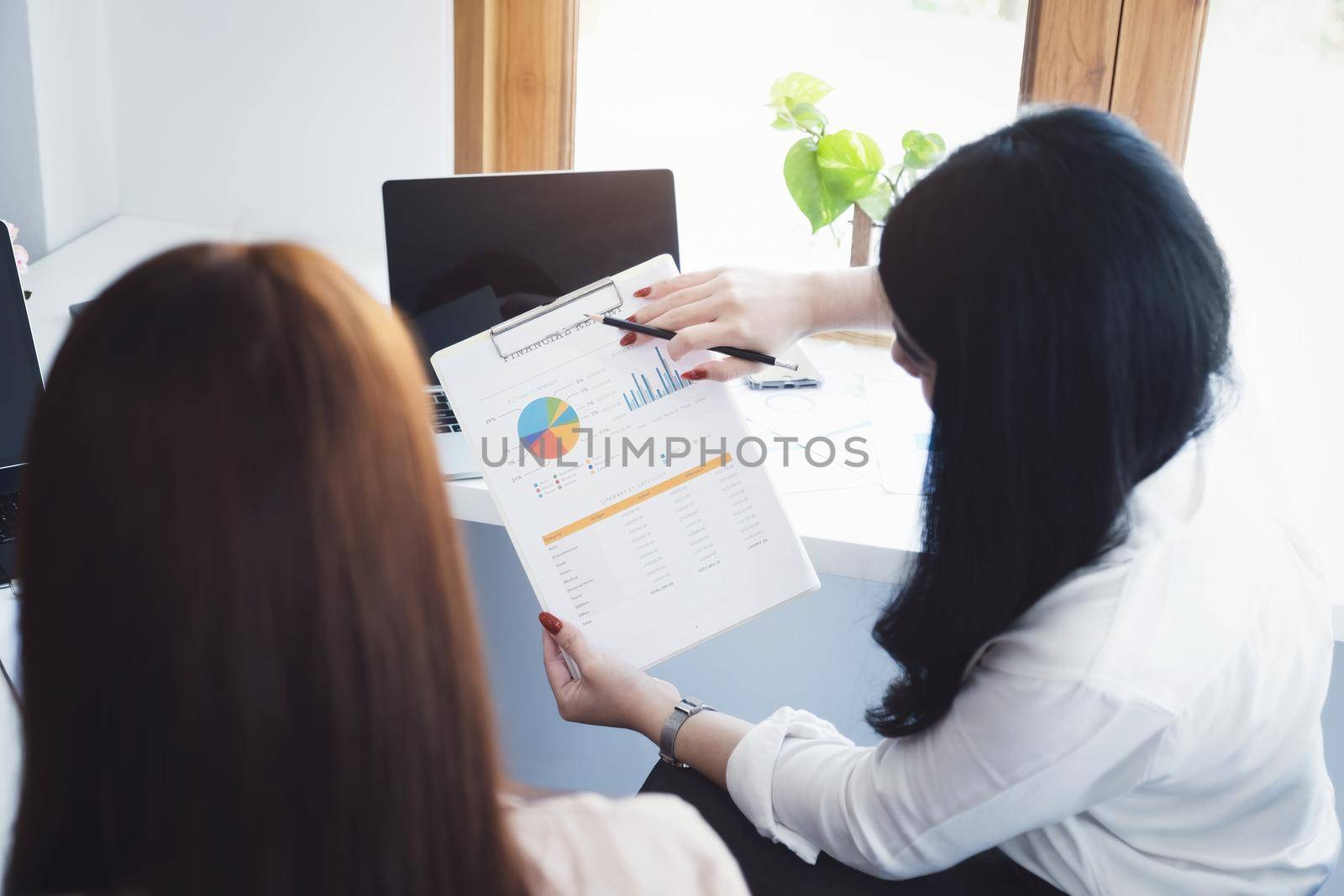 Negotiation, Analysis, Discussion: Portrait of an Asian woman economist and marketer pointing to a financial data sheet to plan investments to prevent risks and losses for the company.