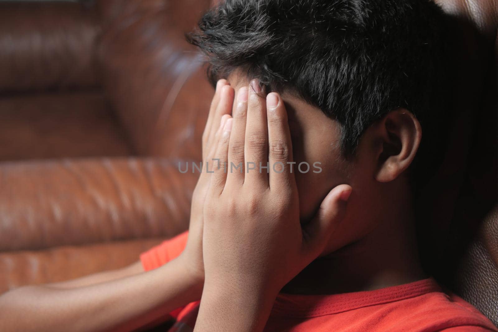 sad teenage boy covering his face sitting on sofa ,