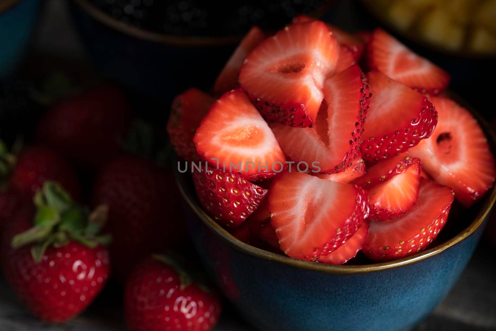 Close up of fresh sliced strawberries in blue bowl low key.