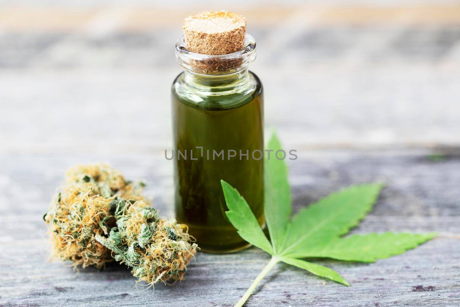 Cannabis oil in a small bottle with bud and leaf on wooden surface
