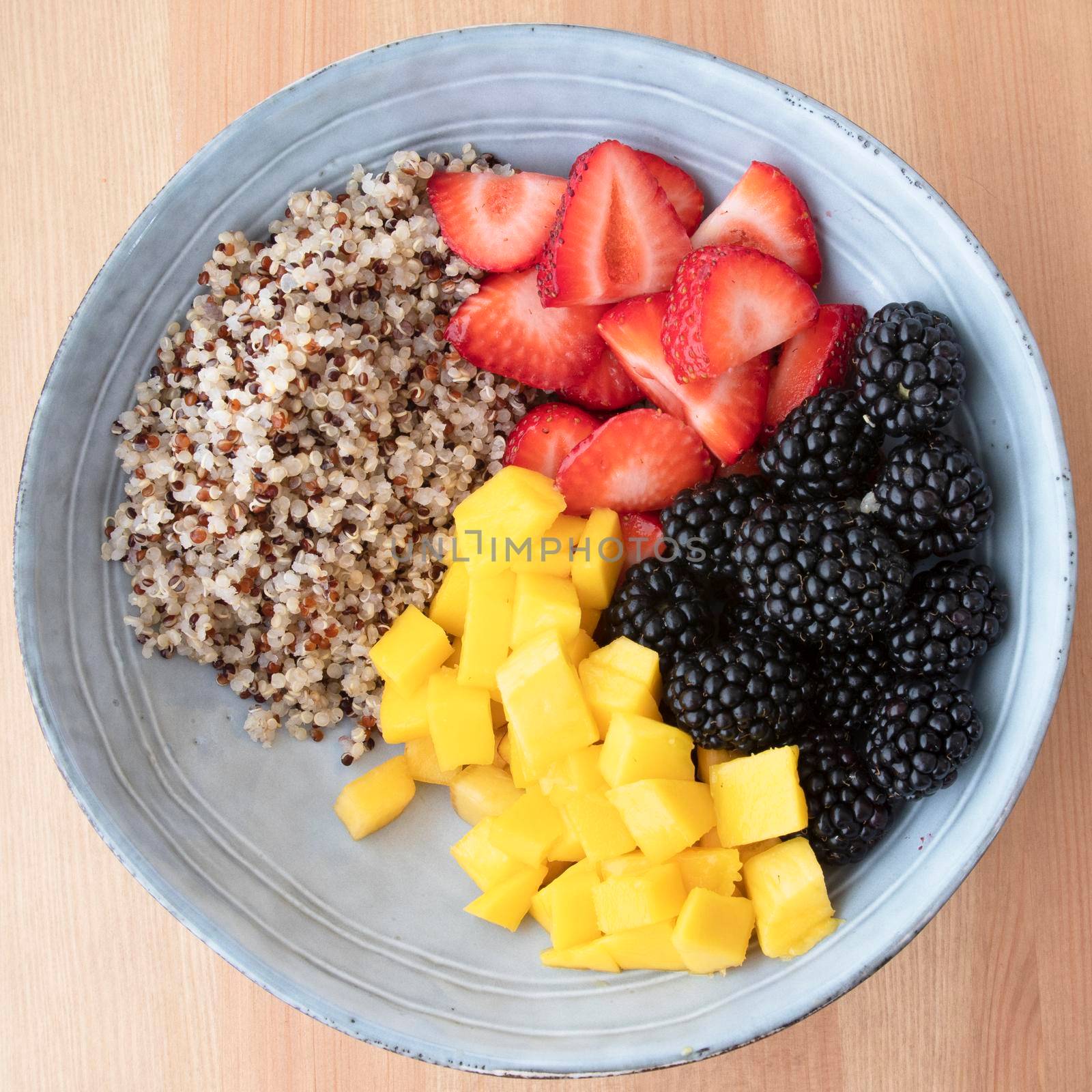 Blue bowl with quinoa, strawberry slices, chopped nectarines and blackberries on wooden surface, image 5 of 8