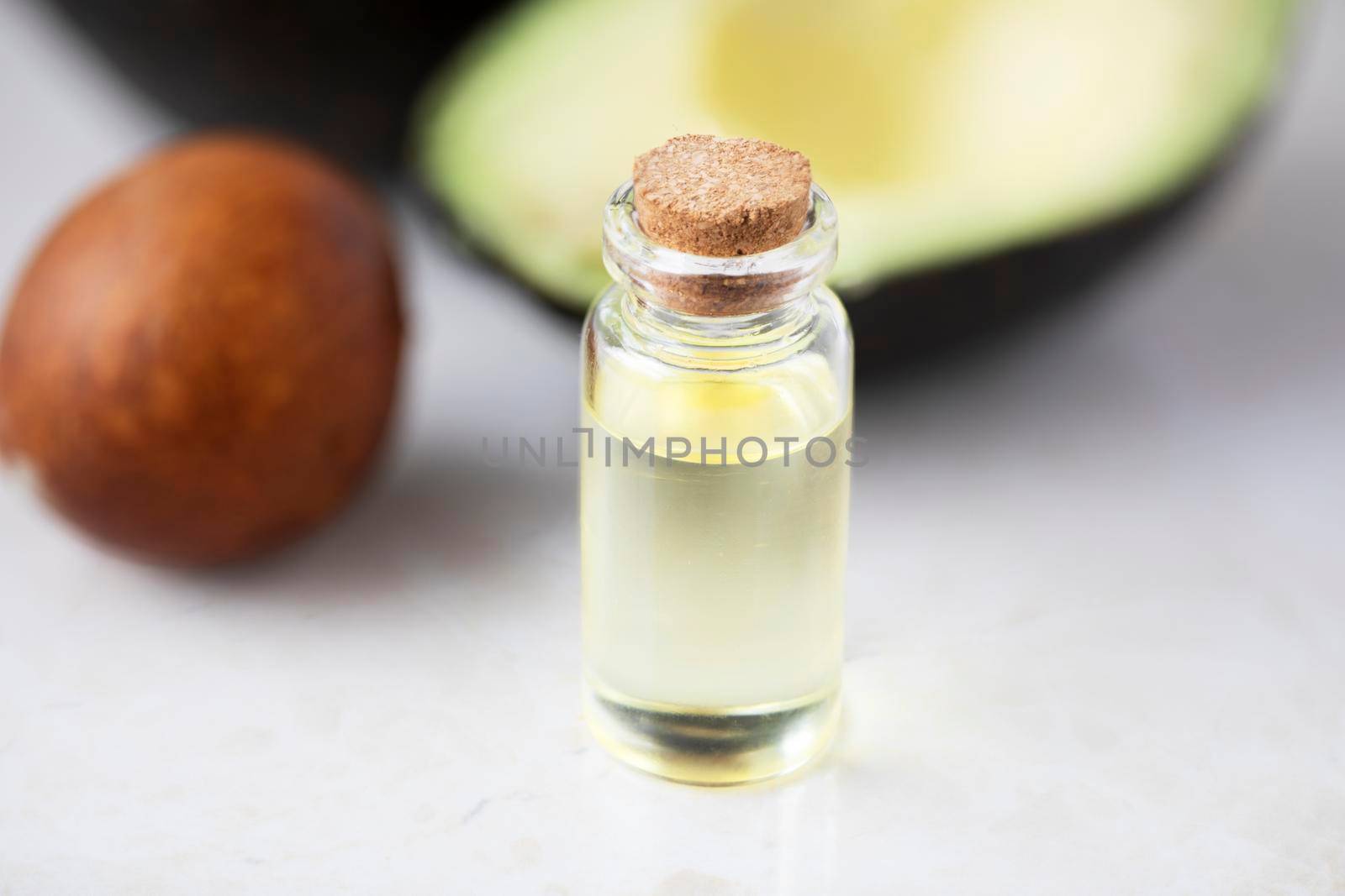 Small bottle of avocado oil and avocados on marble surface
