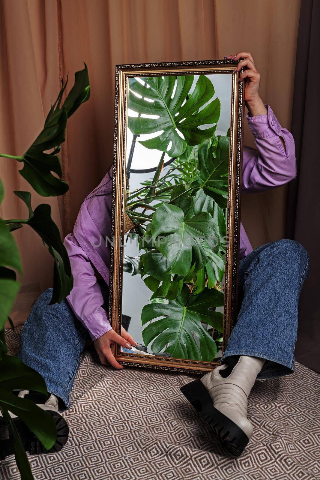 Jungles in the mirror. Woman holds mirror reflecting home jungles with Monstera plant.