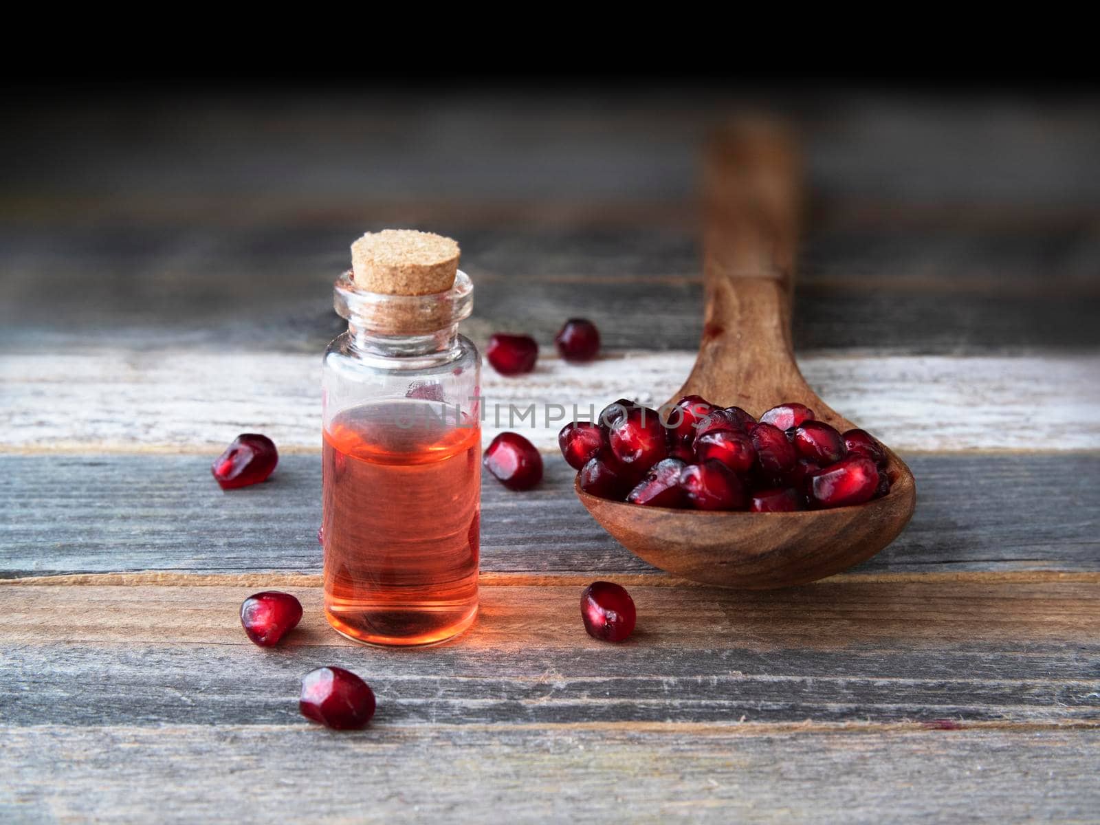 Wooden spoon full o pomegranate seeds and a small bottle of pomegranate extract.
