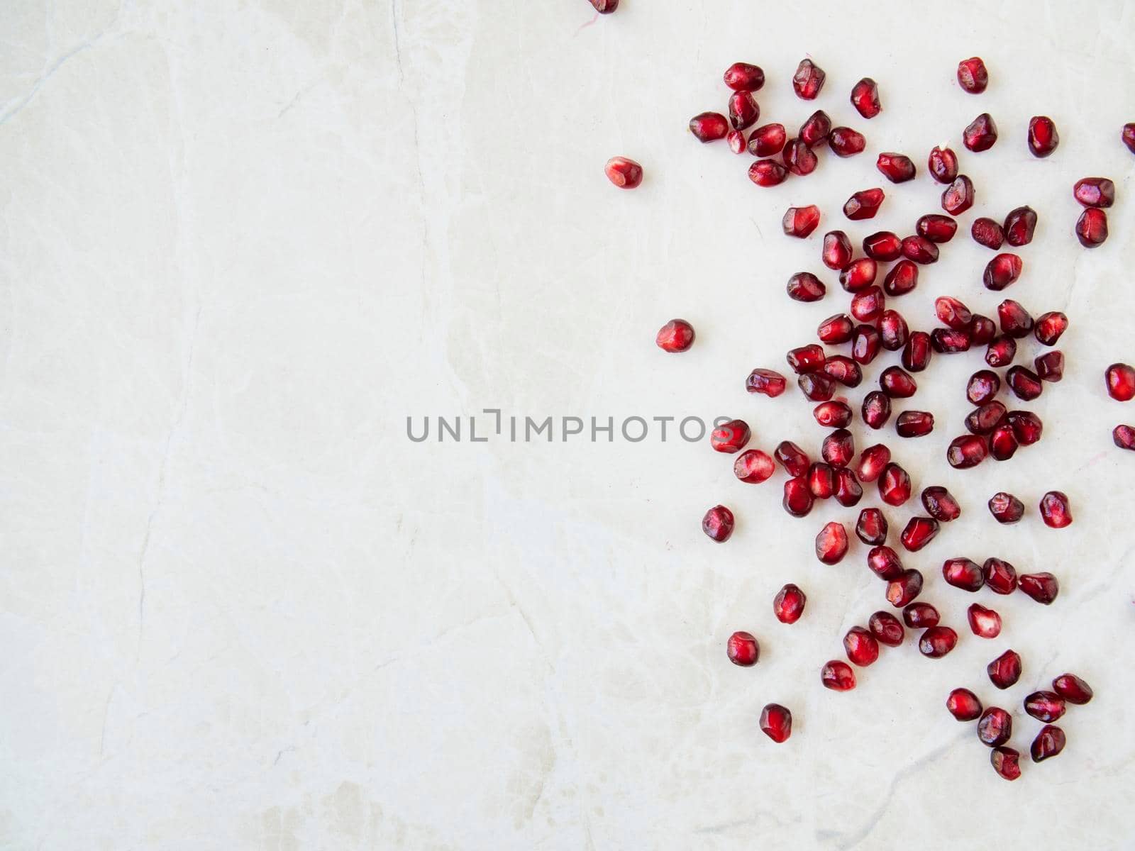 Flat lay pomegranate seeds on marble surface with copy space.