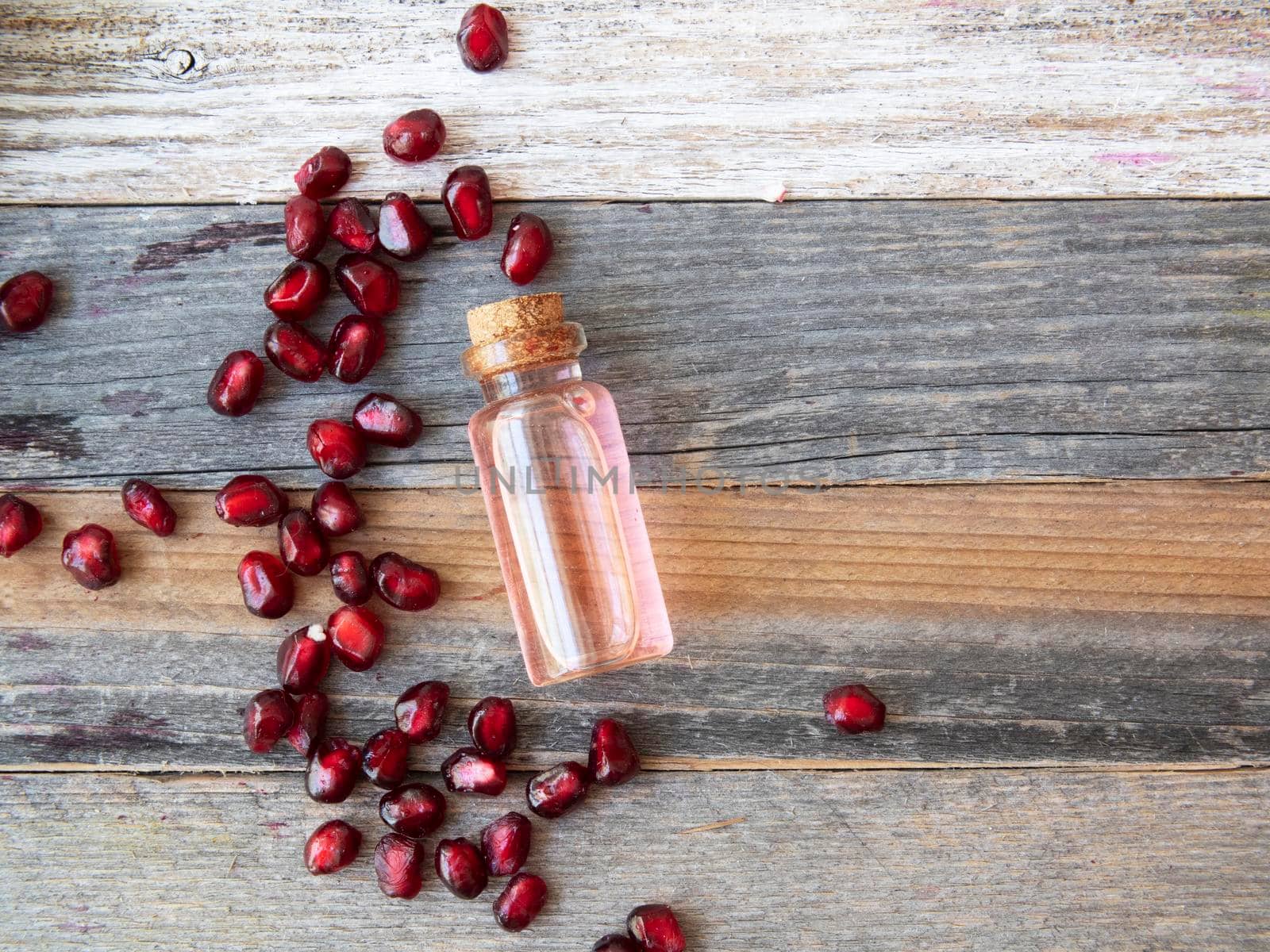 Pomegranate seeds and a small bottle of pomegranate extract on rustic wooden surface with copy space.
