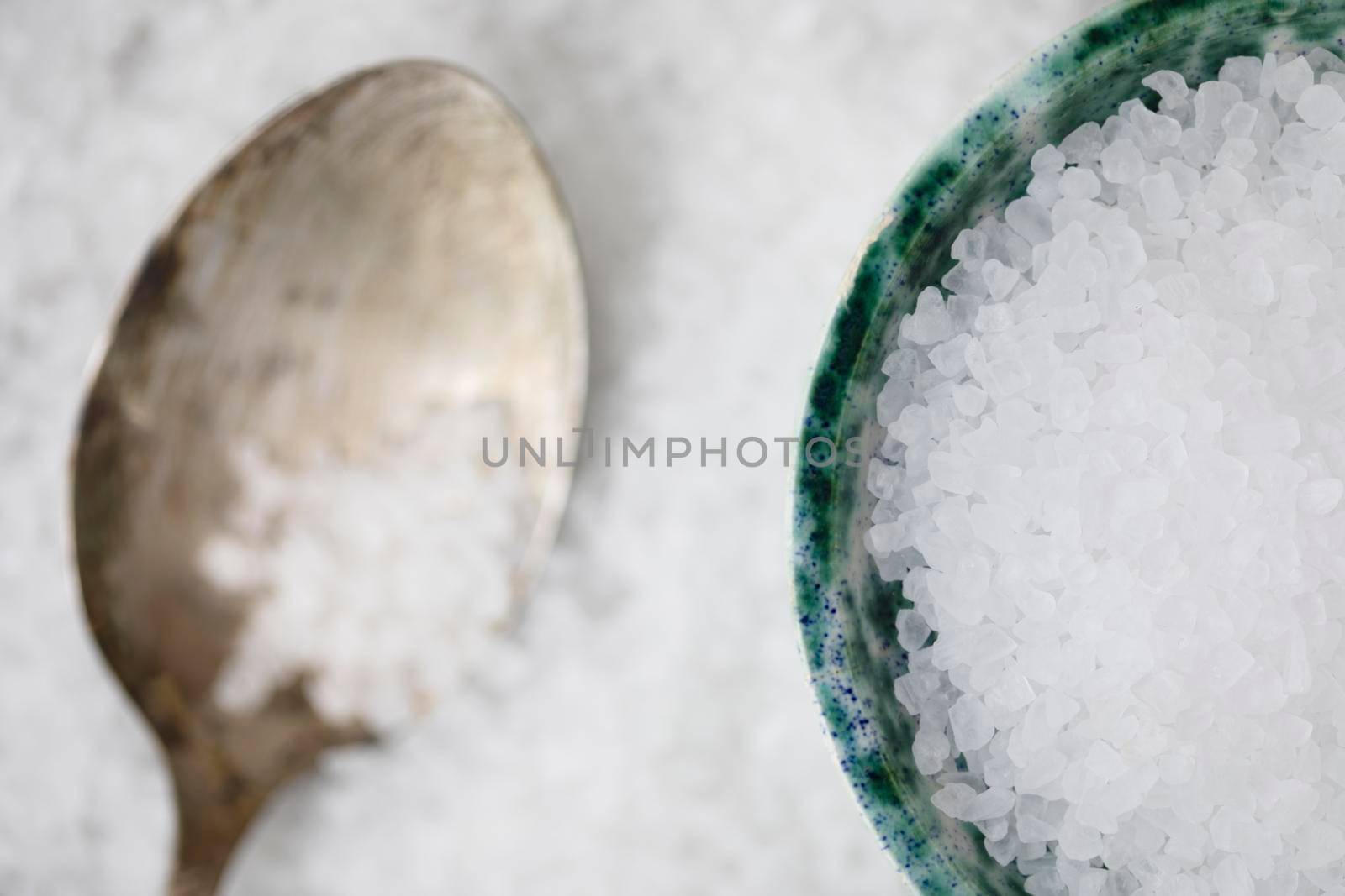Salt crystals in green bowl with spoon on bed of salt.