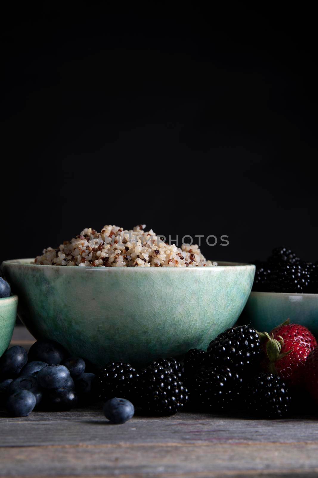 Bowl of healthy quinoa and fresh berries in green bowls, low key lighting and vertical orientation