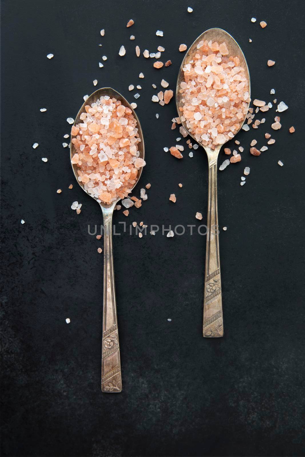 Pink Himalayan salt in old spoons on black background.