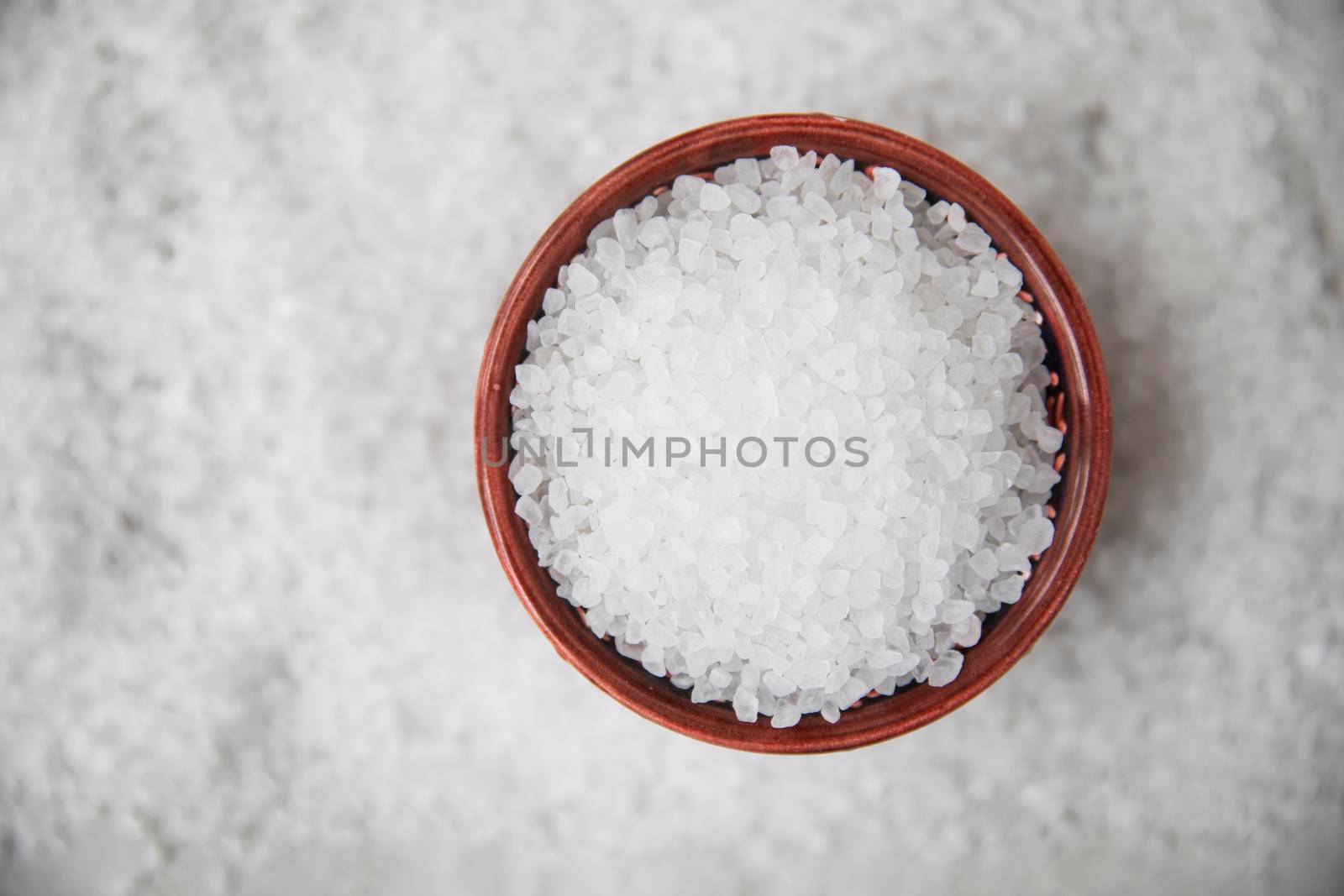 Salt crystals in bowl on bed of salt, flat lay.