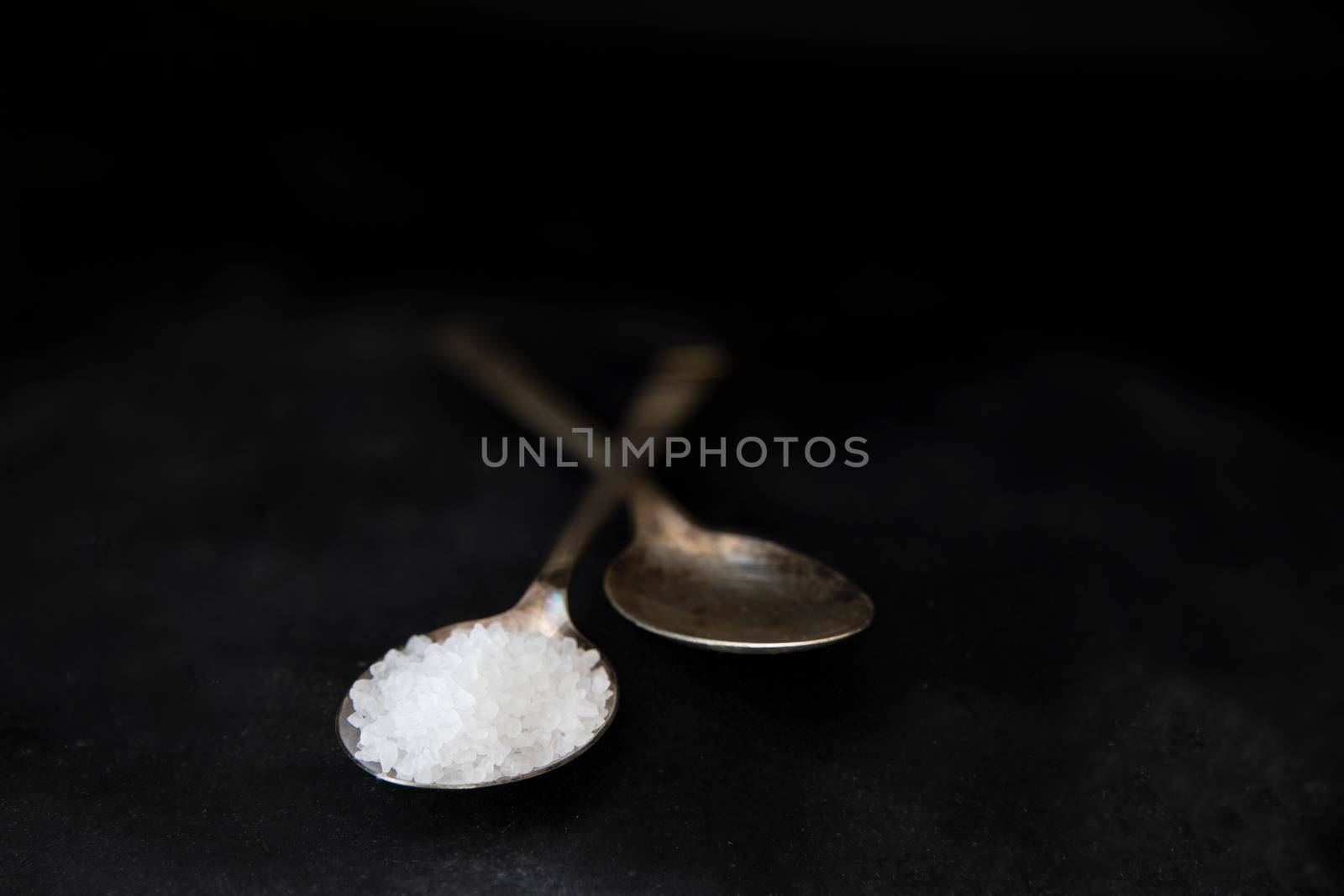 Salt crystals in metal spoons on black background.