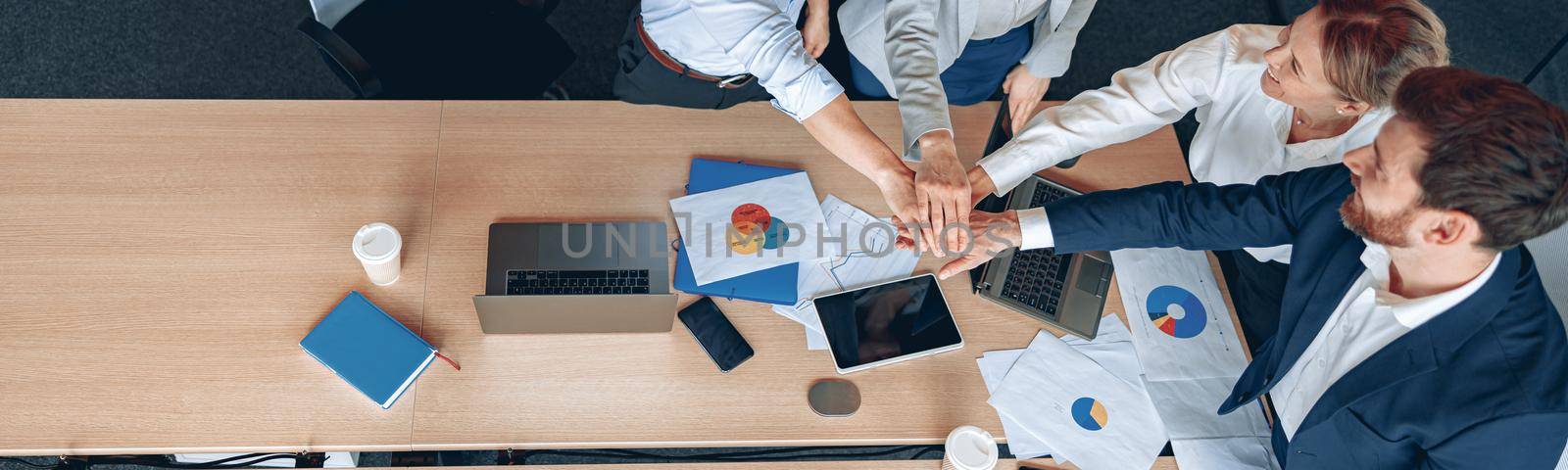 Diverse business people group put hands together while standing near the table in office.