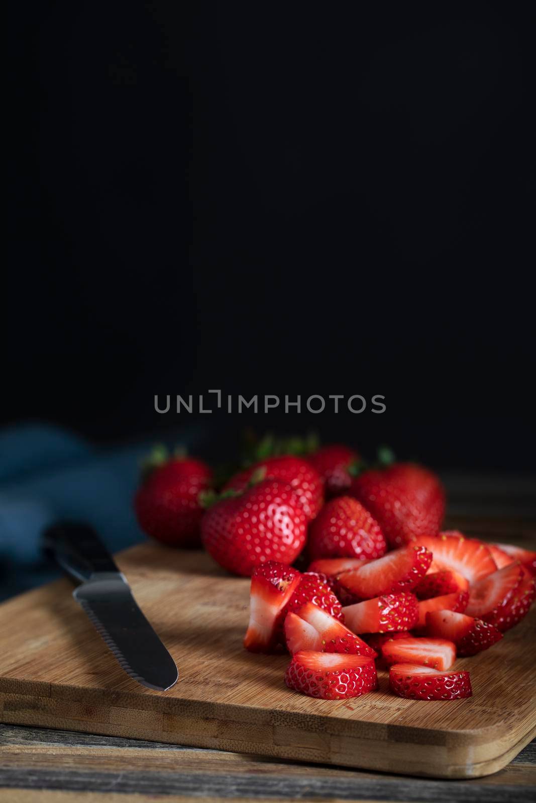 Sliced and whole strawberries on cutting board with knife, low key lighitng and vertical orientation.