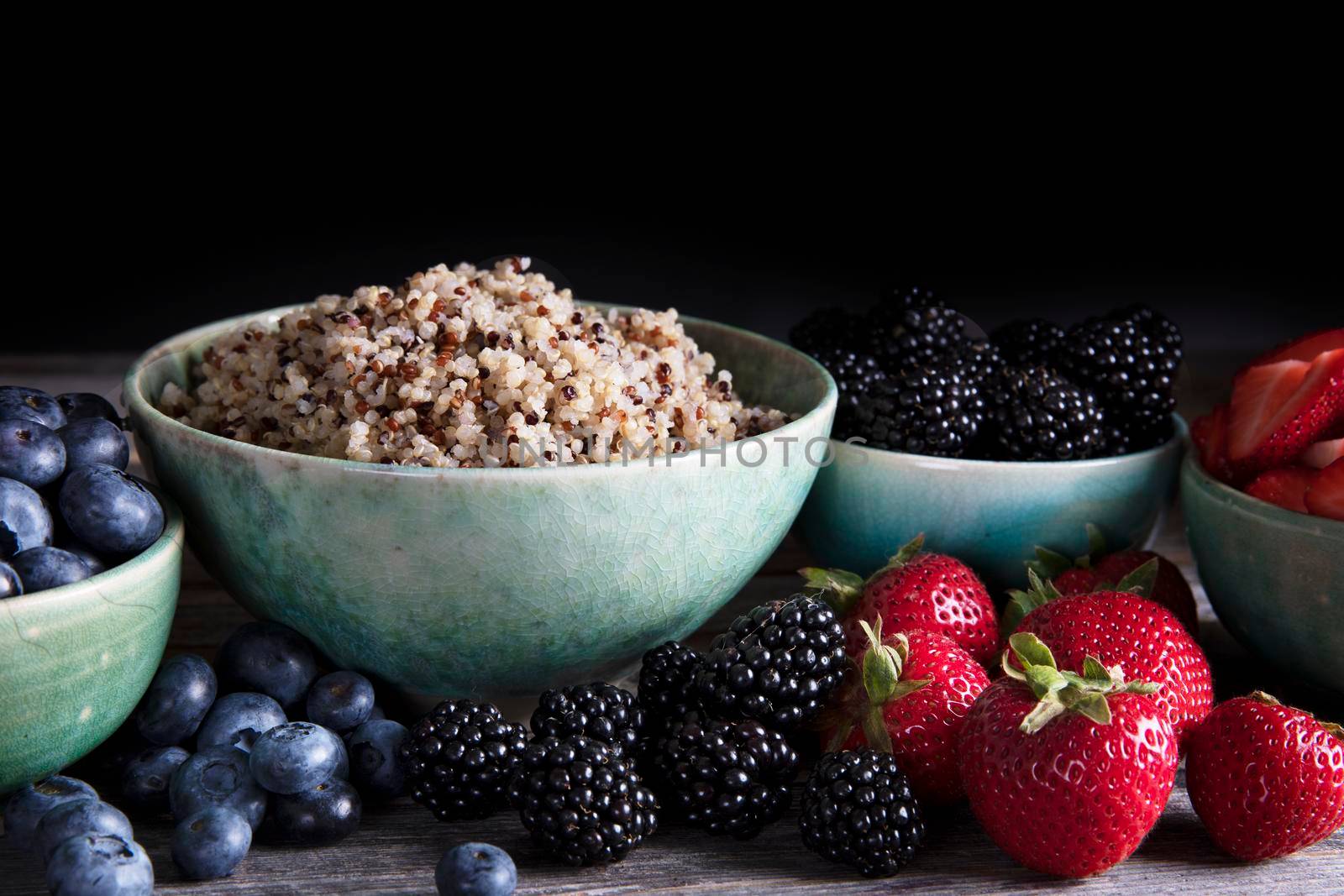 Bowl of healthy quinoa and fresh berries in green bowls, low key lighting and horizontal orientation