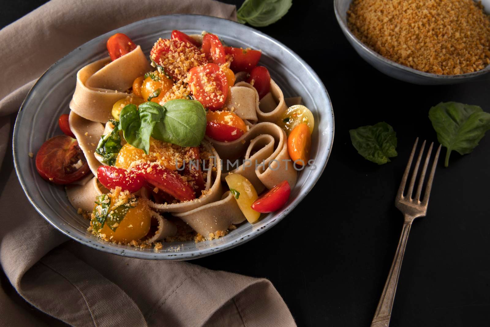 Healthy whole wheat pappardelle pasta with fresh tomatoes and basil, and a vegan nut based topping.