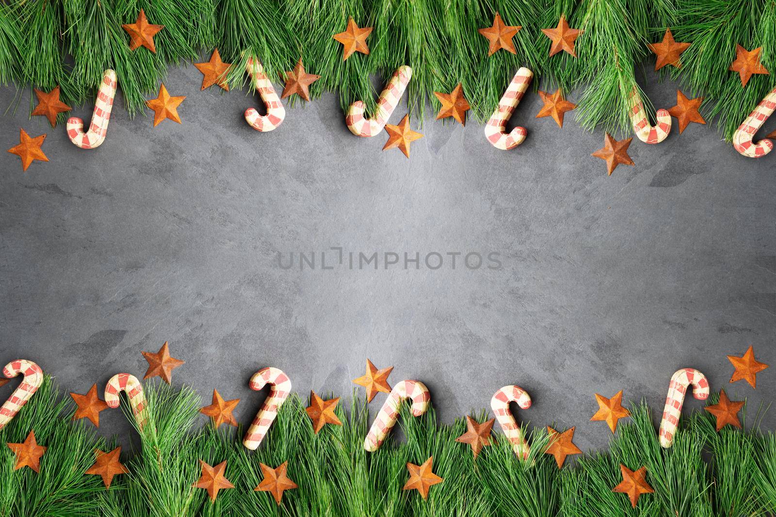 Christmas border of pine boughs, rustic stars and wooden candy canes on slate surface, copy space in the middle.