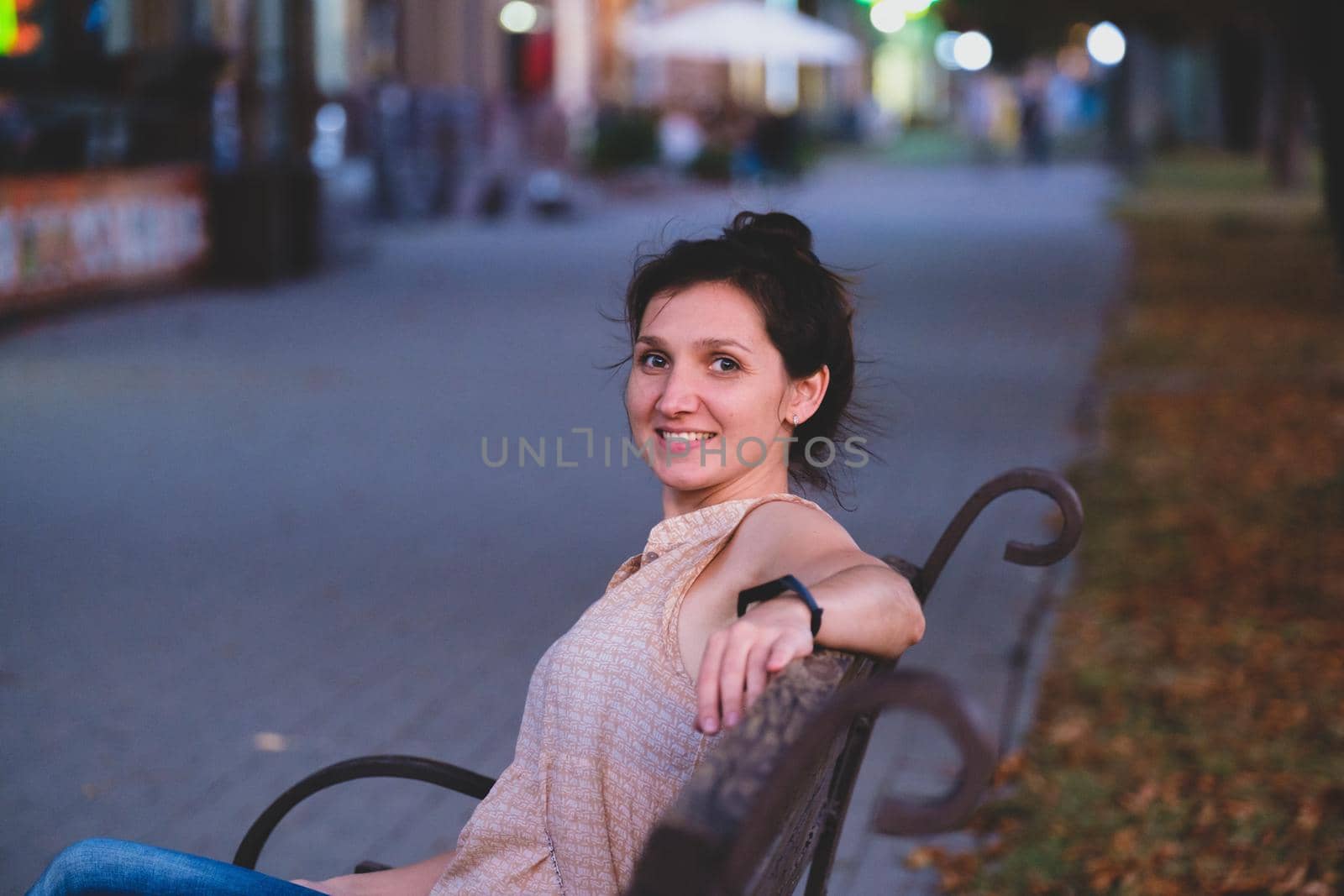 Portrait of a smiling young woman. Elegant european woman sitting on bench. Outdoor portrait of amazing white girl in evening.