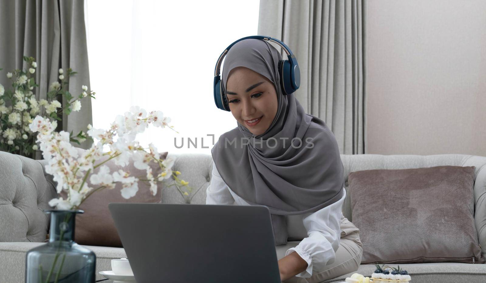 Online Tutoring. Young muslim woman teacher having video call with students, talking at laptop camera, sitting on couch at home.