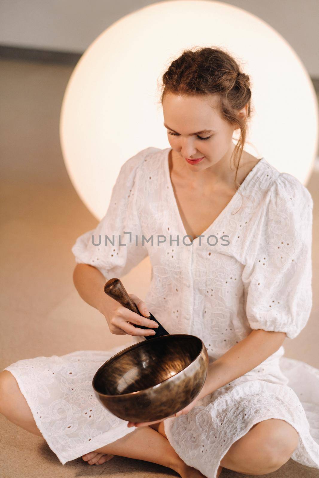 Portrait of a female yoga teacher playing a Tibetan bowl or singing a bell in the gym during a yoga retreat.