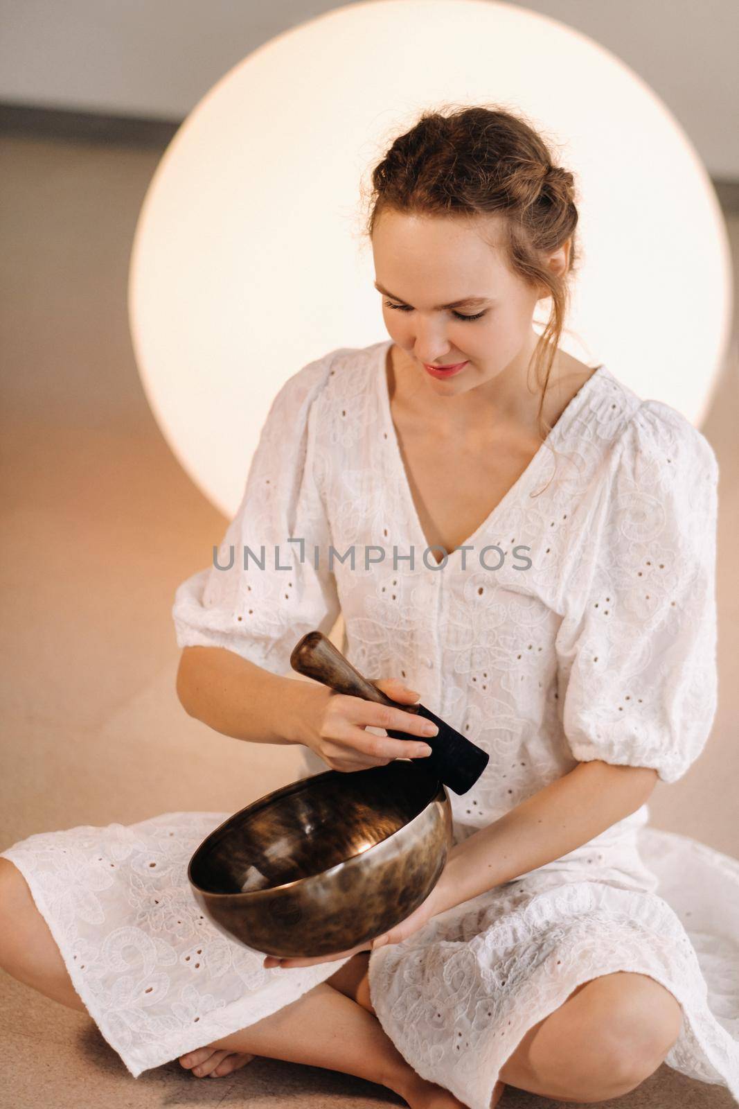 Portrait of a female yoga teacher playing a Tibetan bowl or singing a bell in the gym during a yoga retreat.