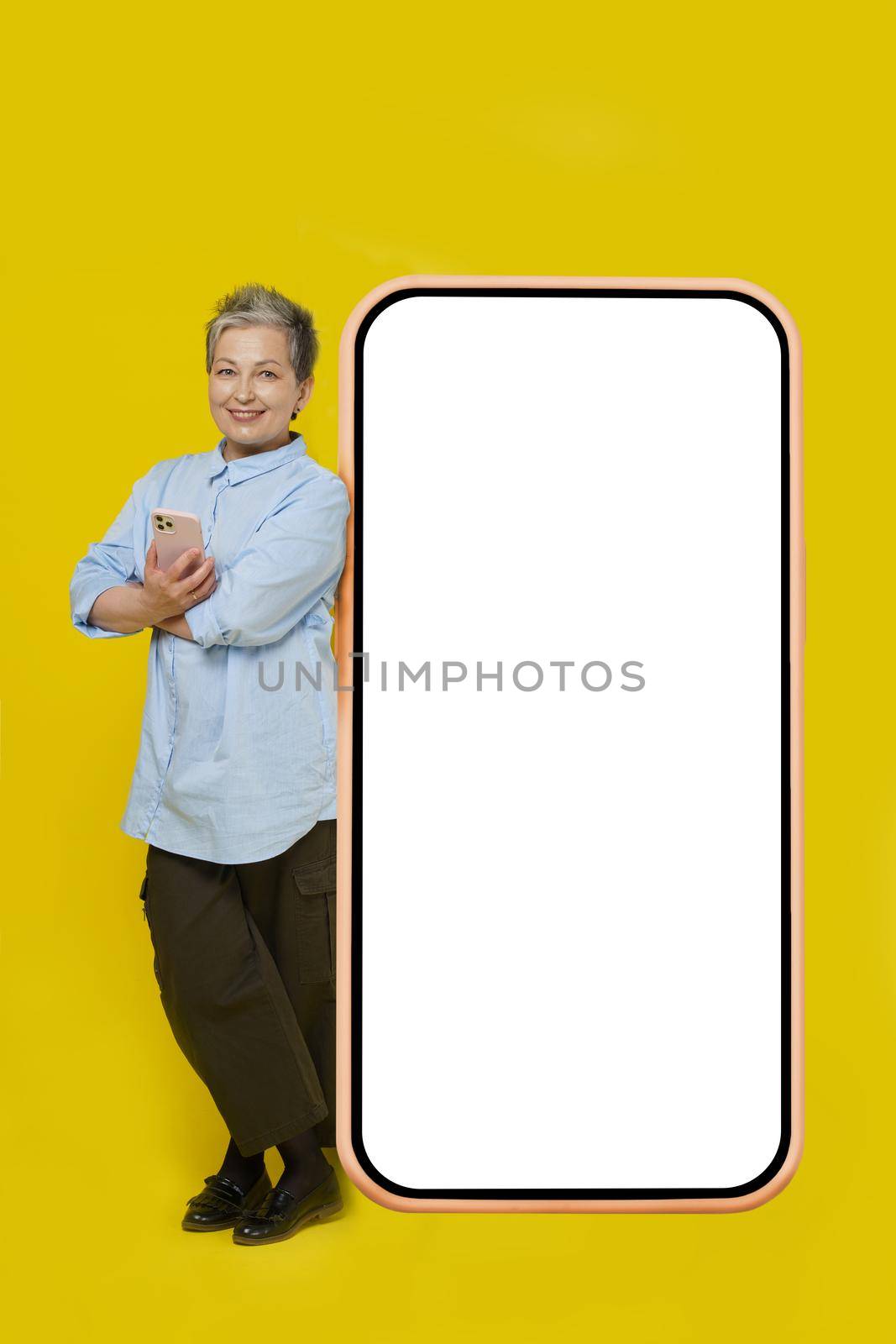 Leaned her back on huge, giant smartphone with white screen grey hair mature business woman with phone in hand looking at camera wearing casual isolated on white background. Free space mock up by LipikStockMedia