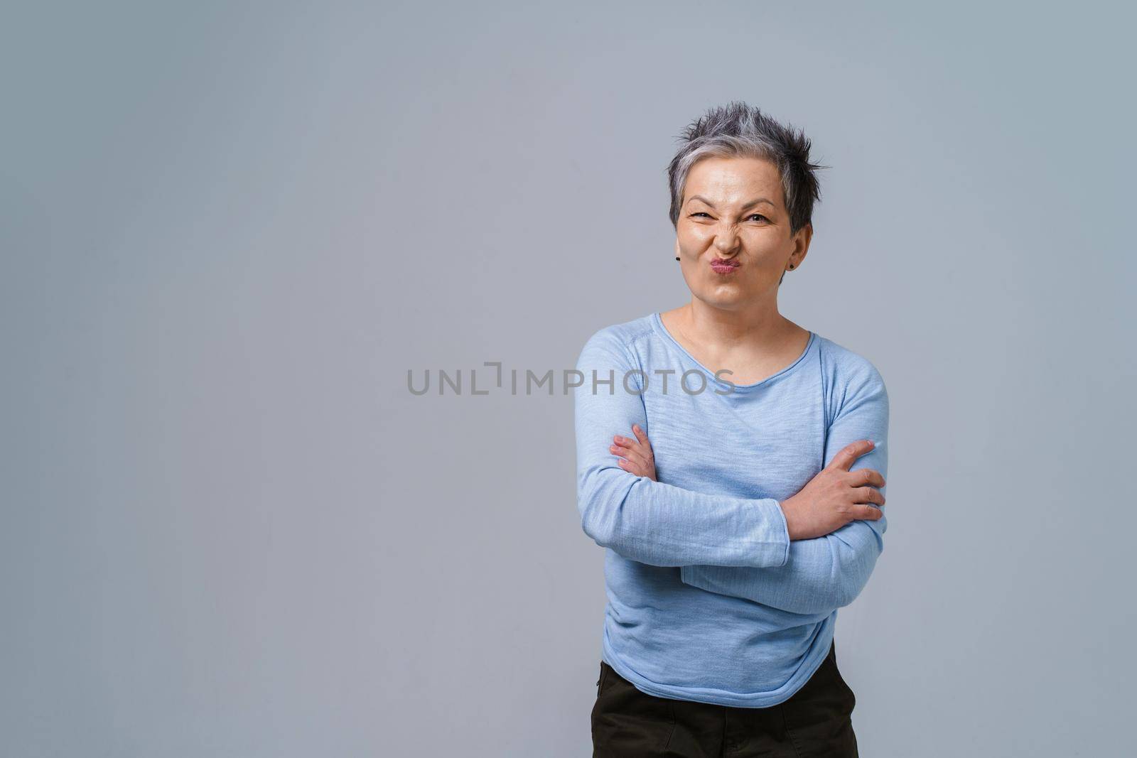 Showing positive dislike on her face mature business woman with grey hair in 50s with hands folded and copy space on left for product placement isolated on white background by LipikStockMedia