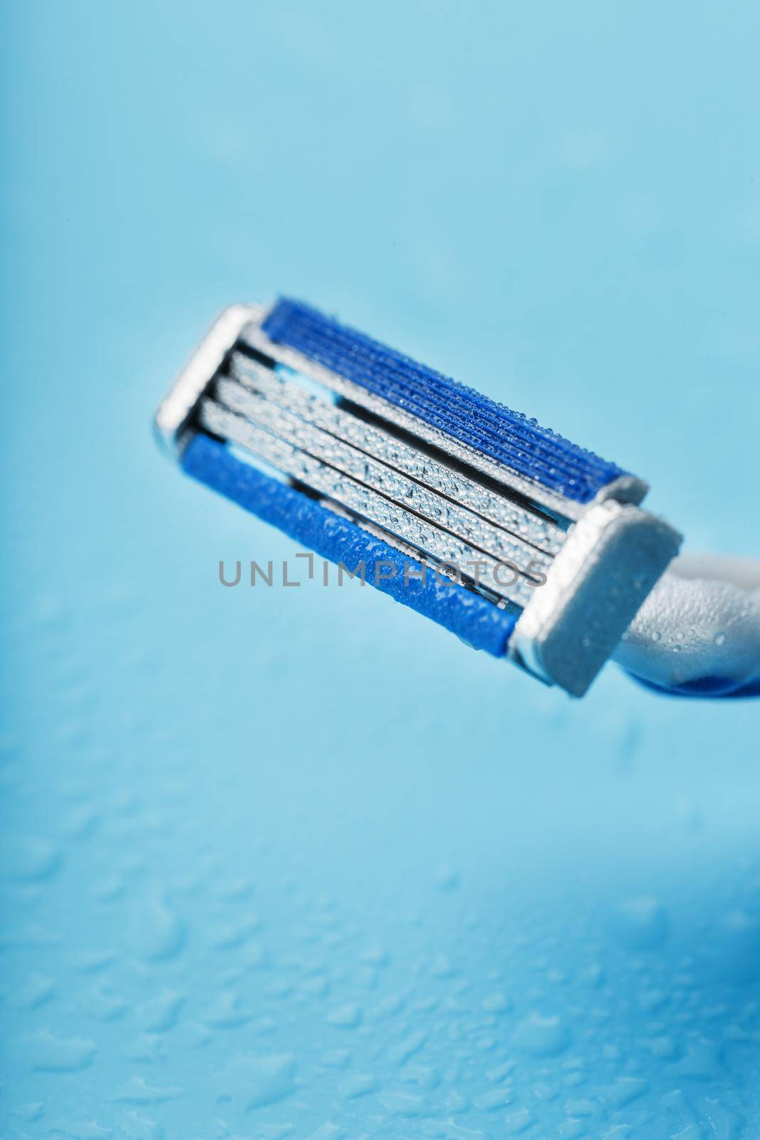 Shaving machine with three blades on a blue background with water drops in close-up. The concept of purity and freshness