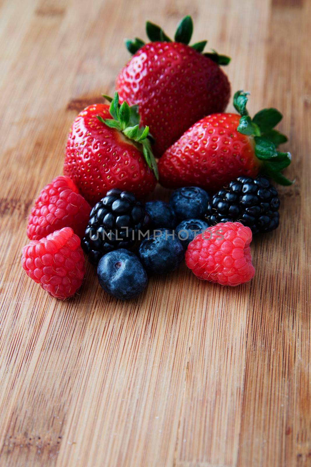Fresh strawberries, blueberries and blackberries on a wooden cutting board