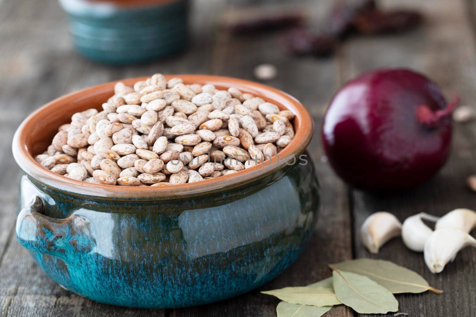 Dried pinto beans in a bowl with bay leaves, garlic and onion on old wooden table.