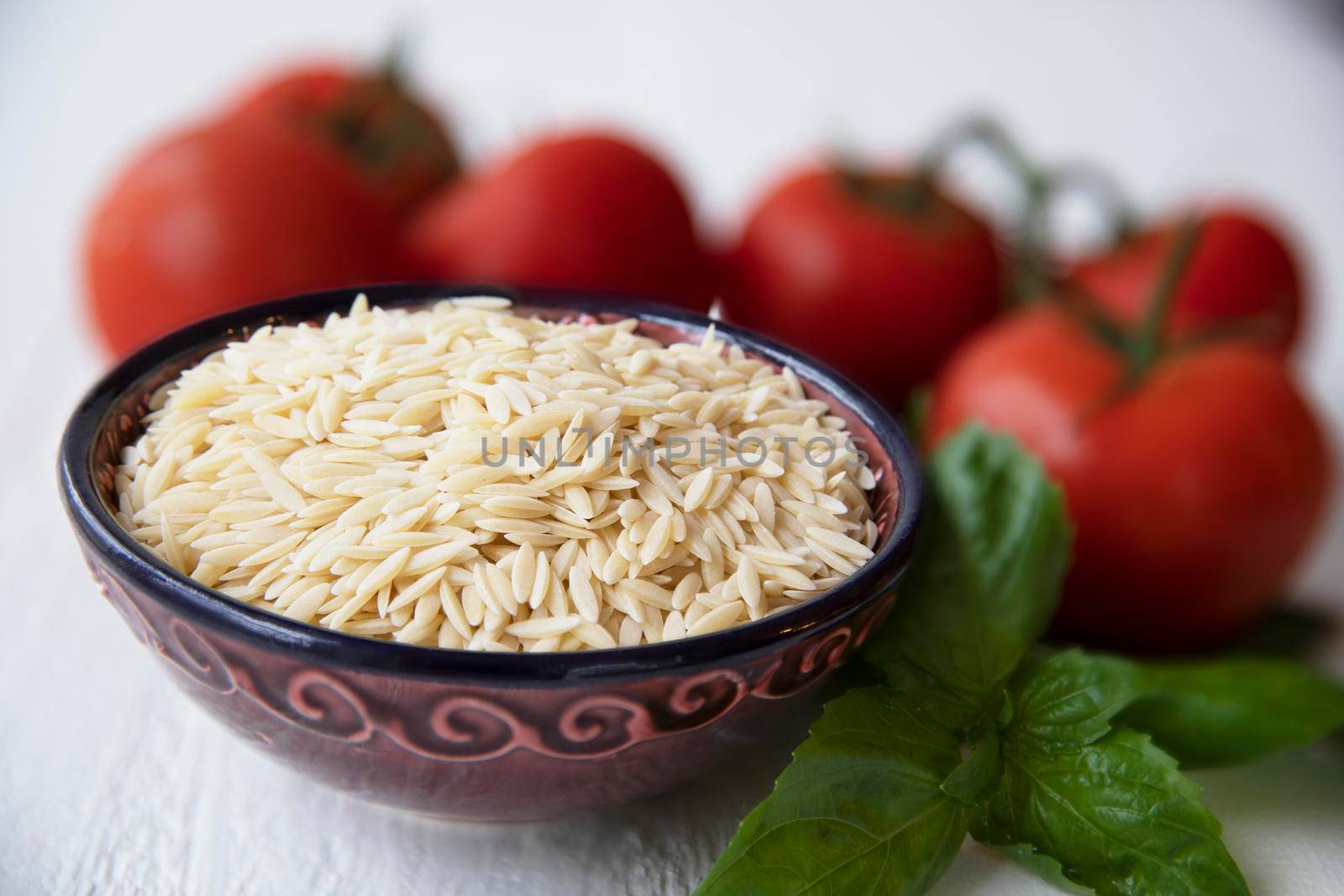 Dried orzo pasta in bowl with basil and tomato