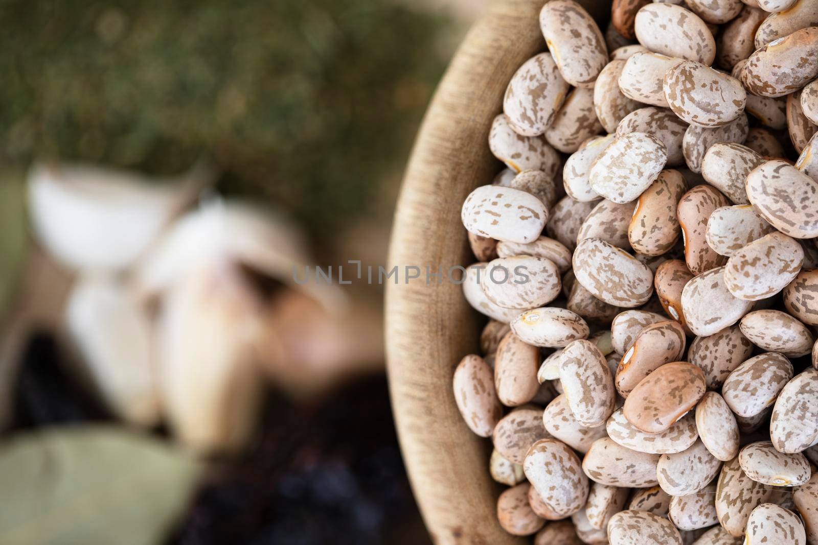 Flat lay of wooden bowl full of dried pinto beans with other spices out of focus on the table.