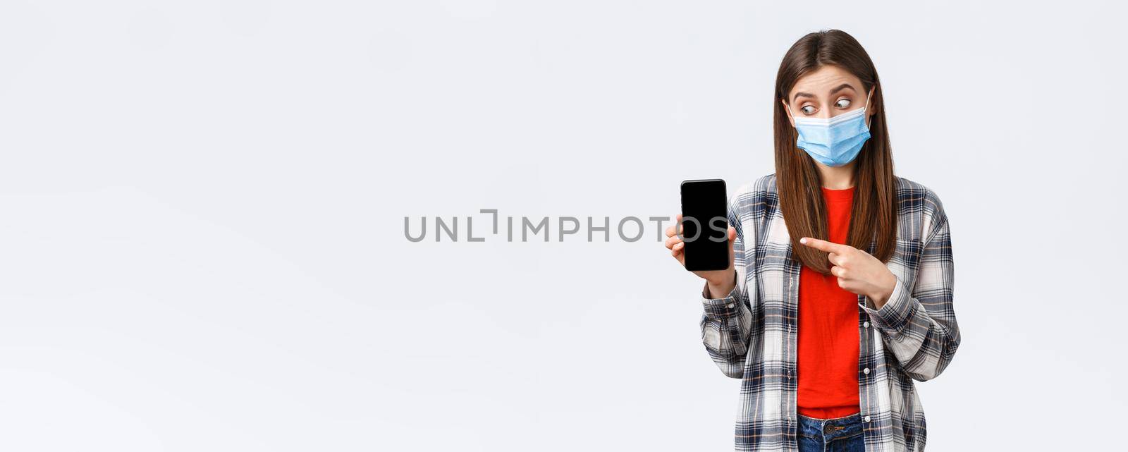 Different emotions, covid-19, social distancing and technology concept. Excited and enthusiastic good-looking girl in medical mask, pointing looking at mobile phone display, promote app by Benzoix