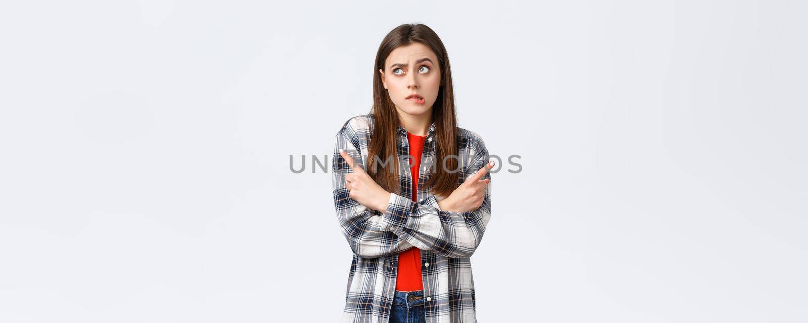 Lifestyle, different emotions, leisure activities concept. Indecisive silly cute girl facing hard choice, cross hands and pointing sideways, leaning to left variant, biting lip confused and puzzled.