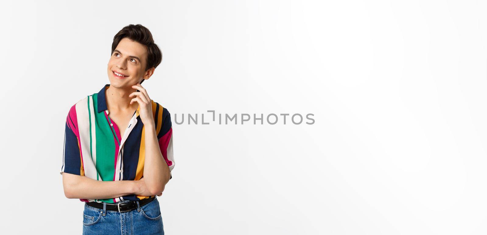 Thoughtful smiling gay man looking at upper left corner, imaging something, standing over white background by Benzoix