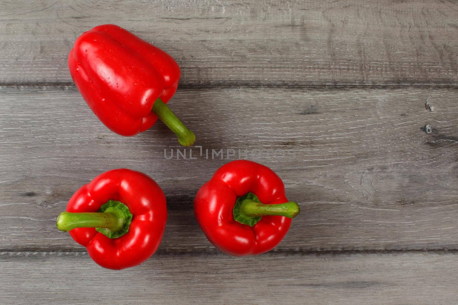 Tabletop view - three red bell peppers on gray wood desk.