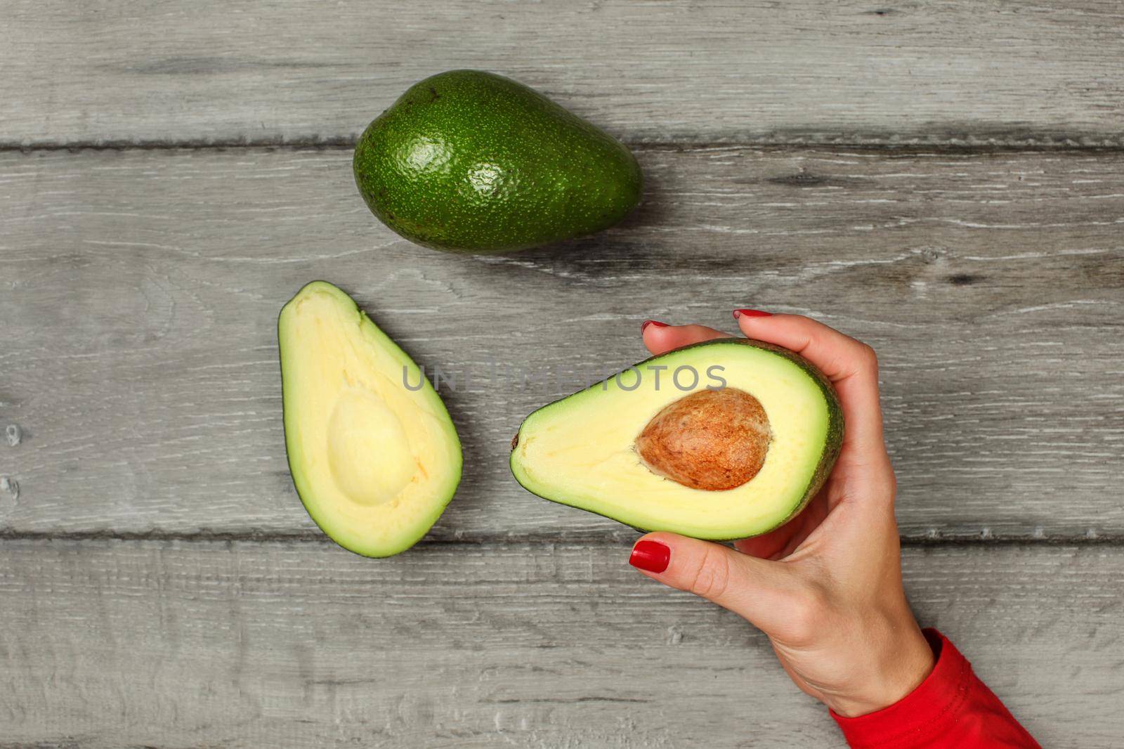 Tabletop view, woman hand holding avocado cut in half with whole pear above.