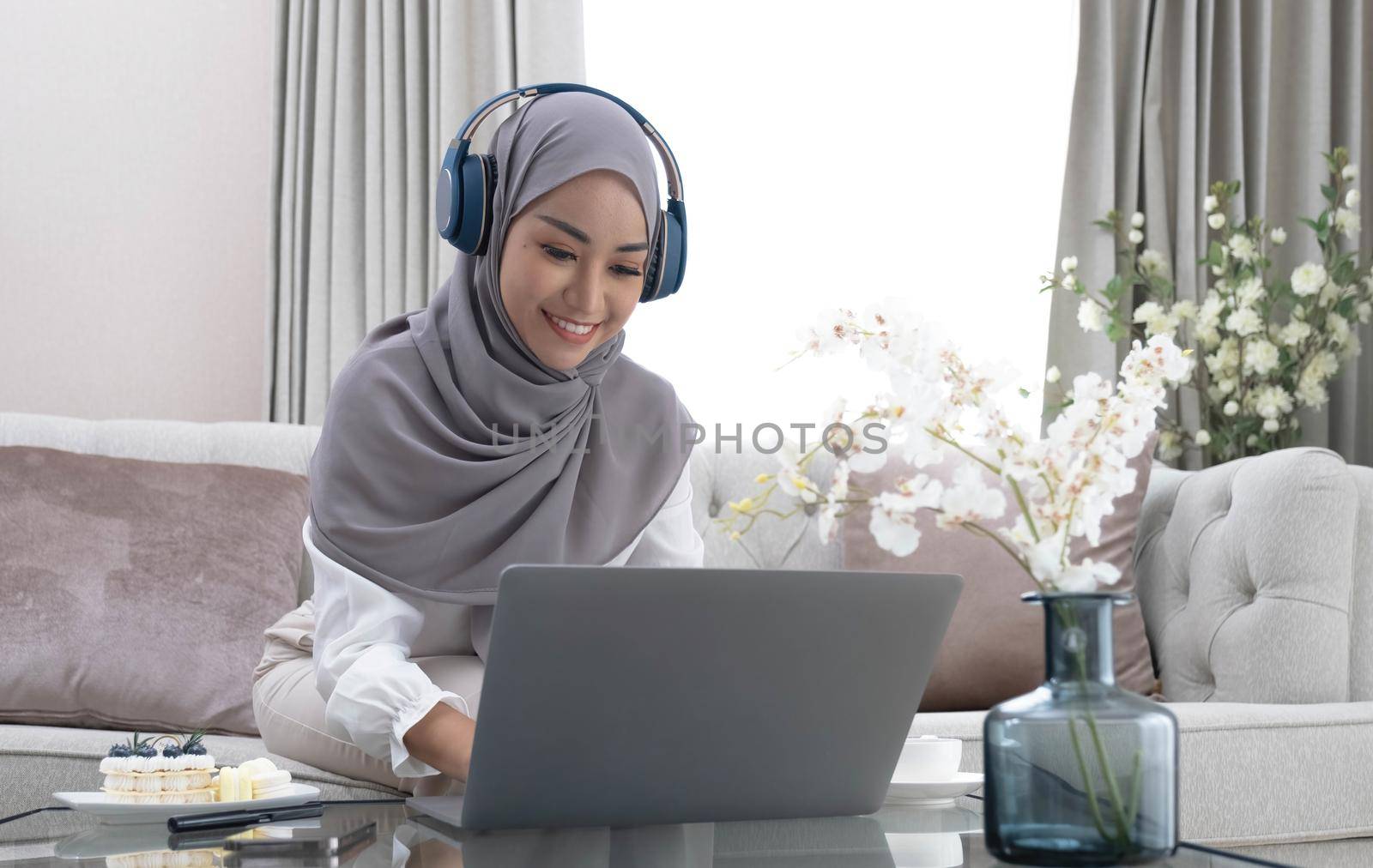 Online Tutoring. Young muslim woman teacher having video call with students, talking at laptop camera, sitting on couch at home.