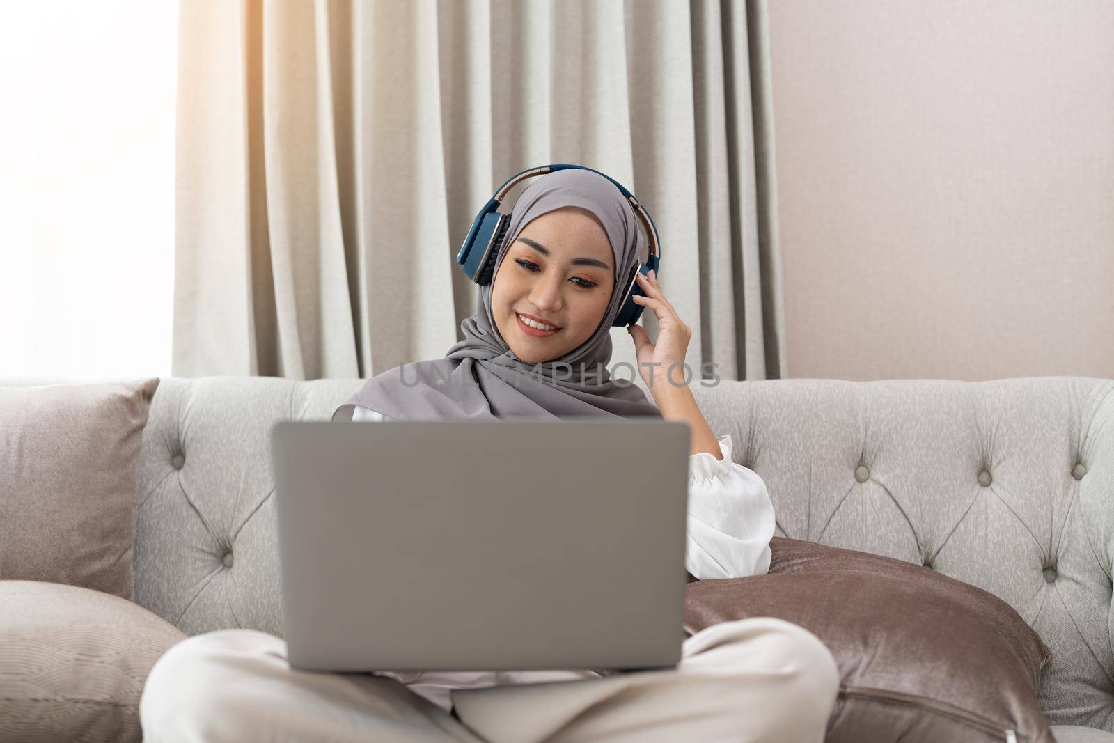 Asian muslim woman having video teleconference on her laptop at home, online learning or working from home concept by nateemee