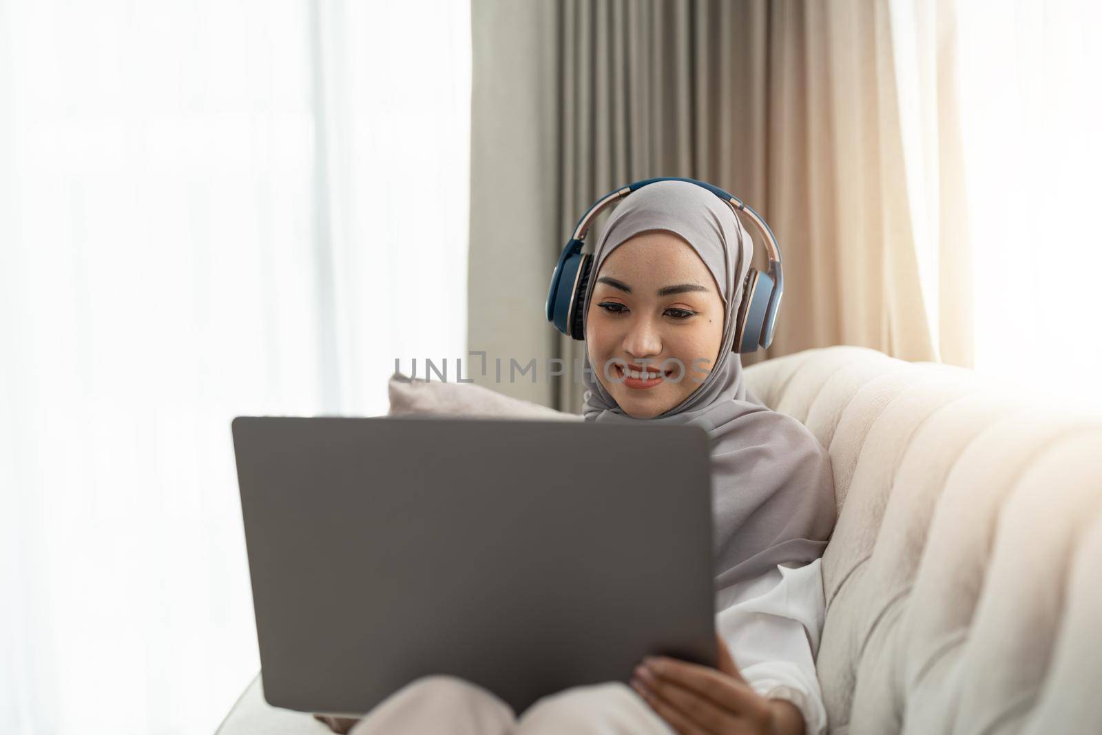 Asian muslim woman having video teleconference on her laptop at home, online learning or working from home concept.