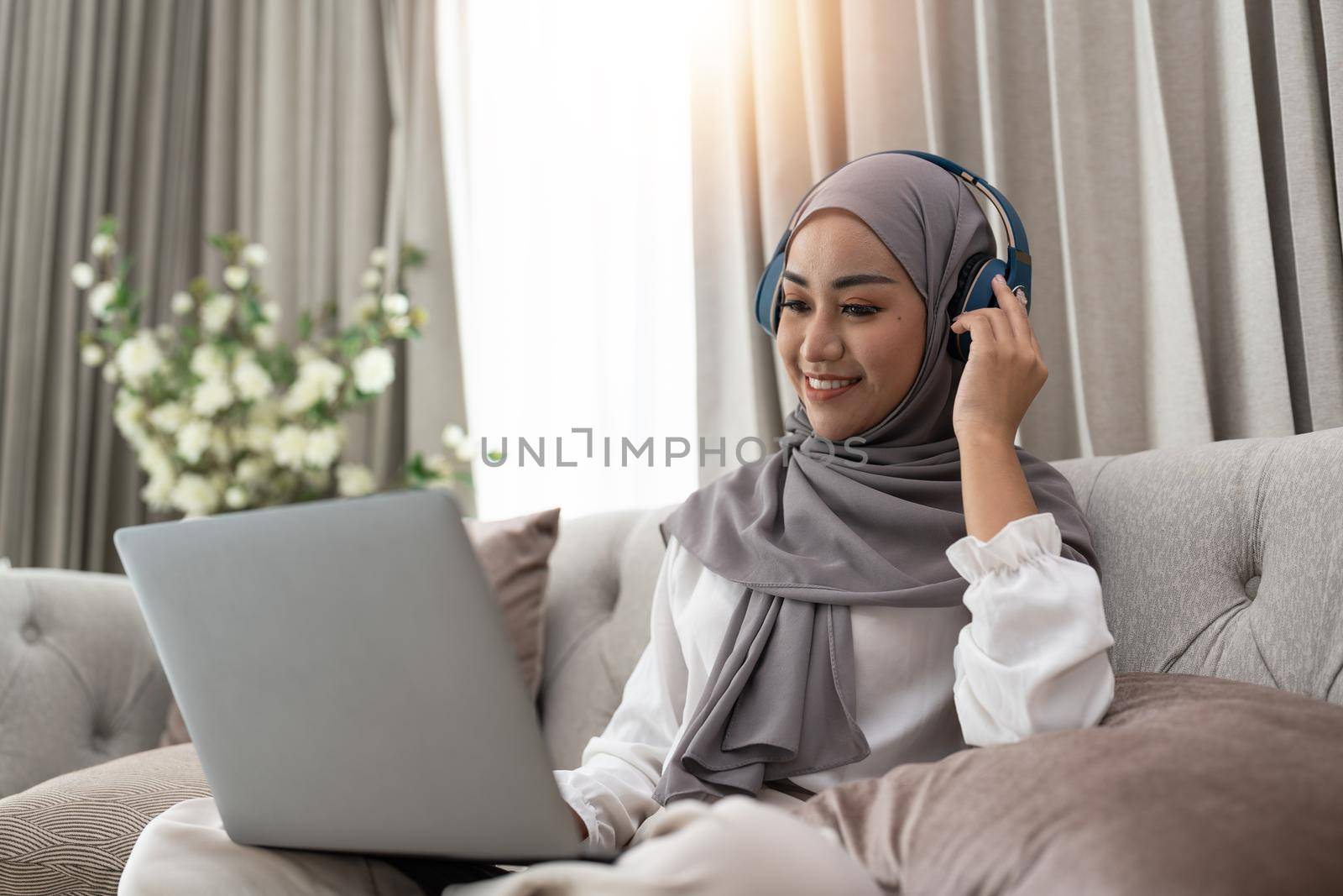 Asian muslim woman having video teleconference on her laptop at home, online learning or working from home concept.