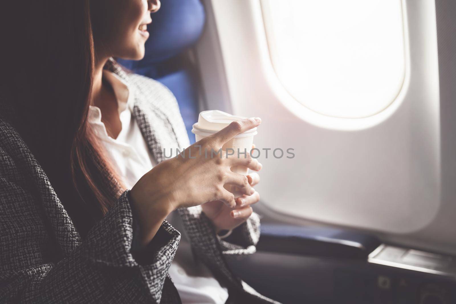A successful asian business woman or female entrepreneur in formal suit in a plane sits in a business class seat and drink coffee during flight, relax concept by Manastrong