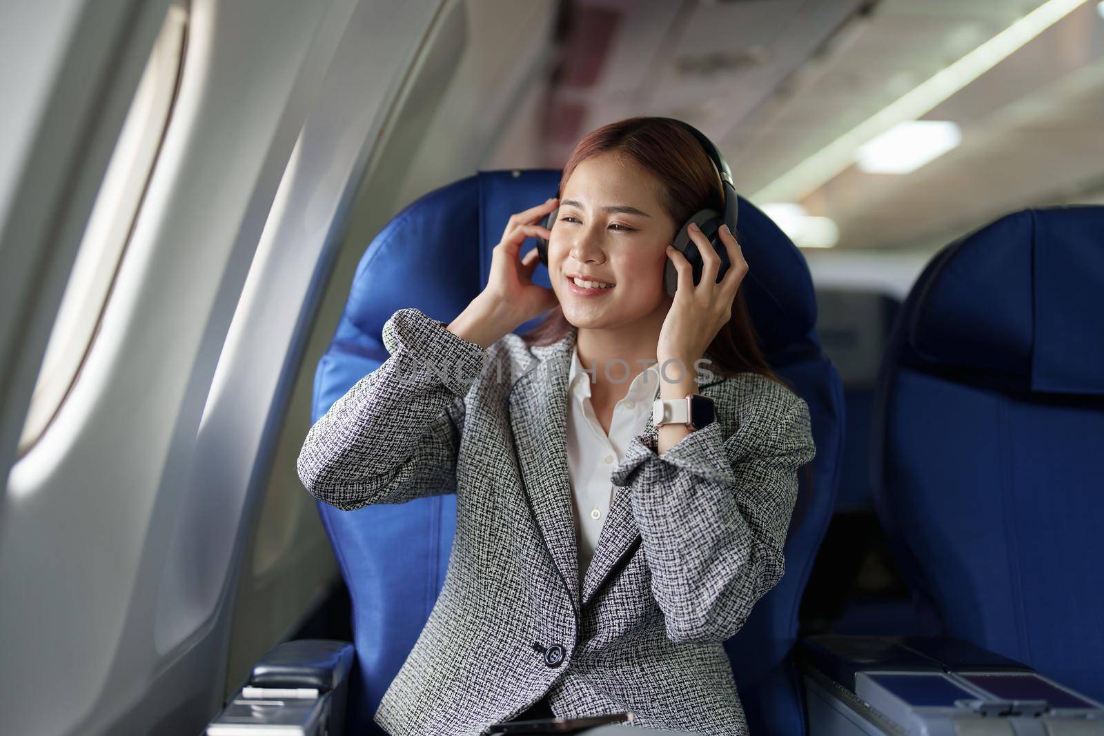 portrait of A successful asian business woman in a plane sits in a business class seat and uses a Around-Ears Headphones for playing music during flight. relax concept.