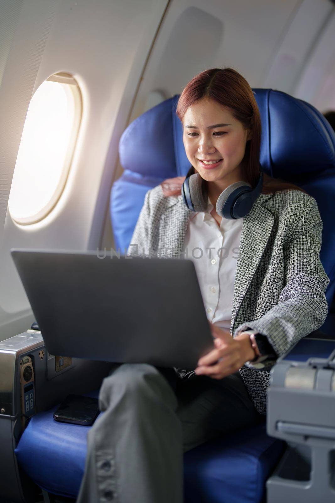 portrait of A successful asian business woman or female entrepreneur in formal suit in a plane sits in a business class seat and uses a computer laptop during flight.