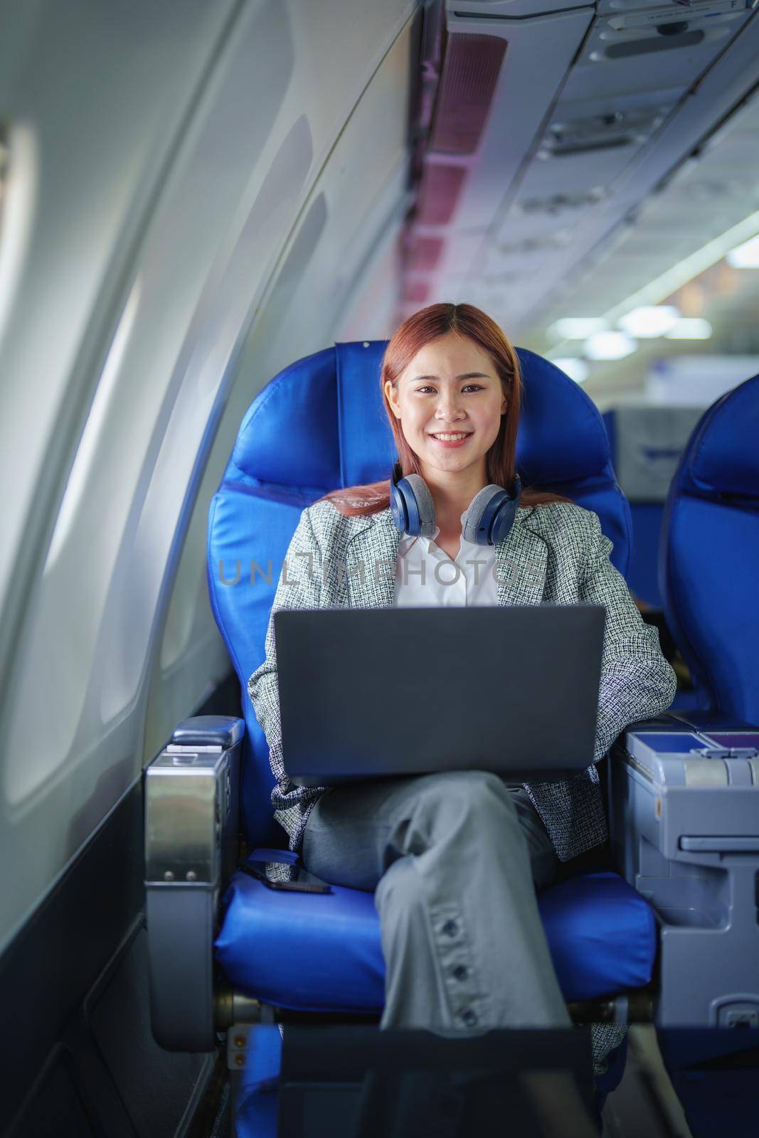 portrait of A successful asian business woman or female entrepreneur in formal suit in a plane sits in a business class seat and uses a computer laptop during flight by Manastrong