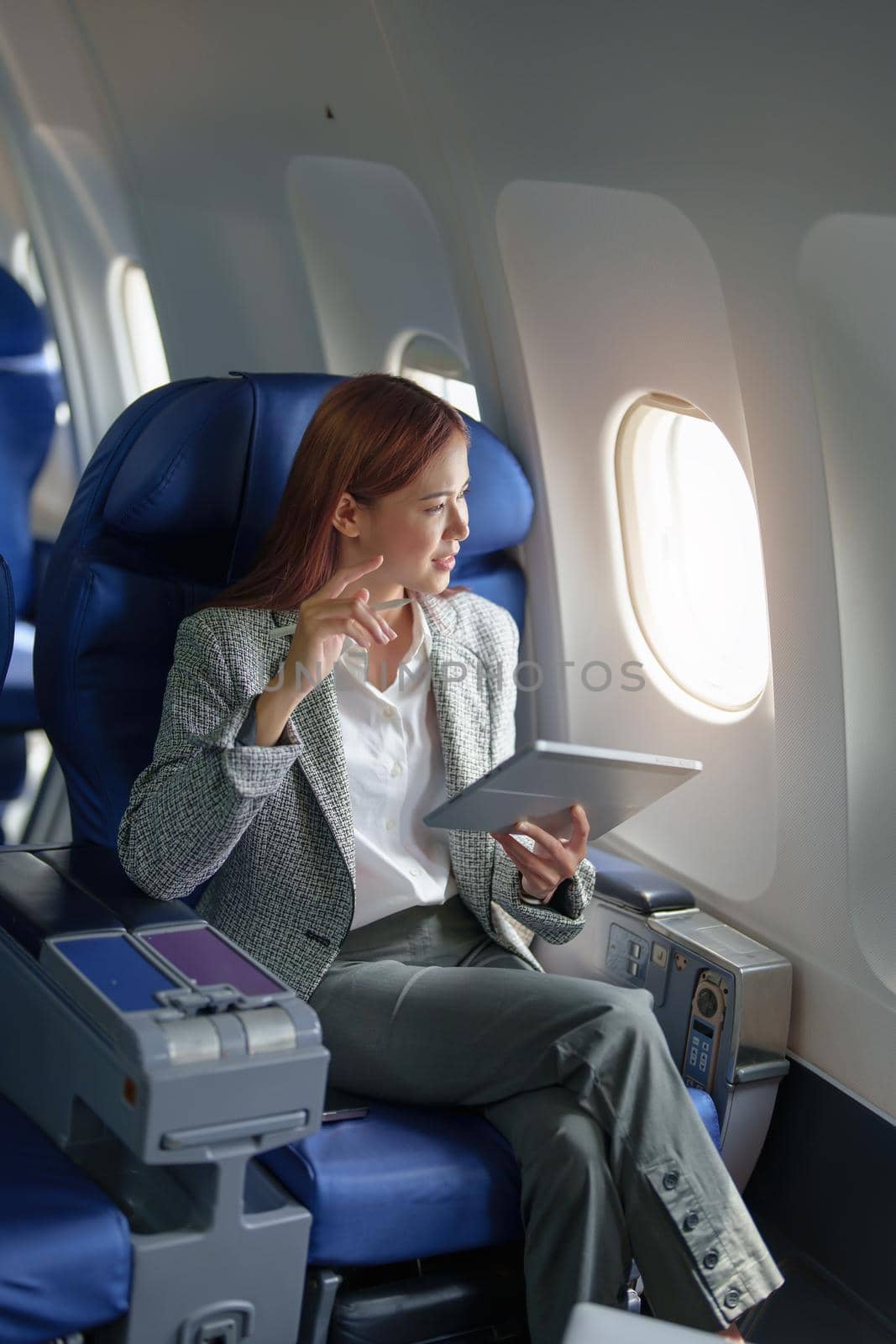 portrait of A successful asian businesswoman or female entrepreneur in formal suit in a plane sits in a business class's seat and uses a tablet computer during flight by Manastrong