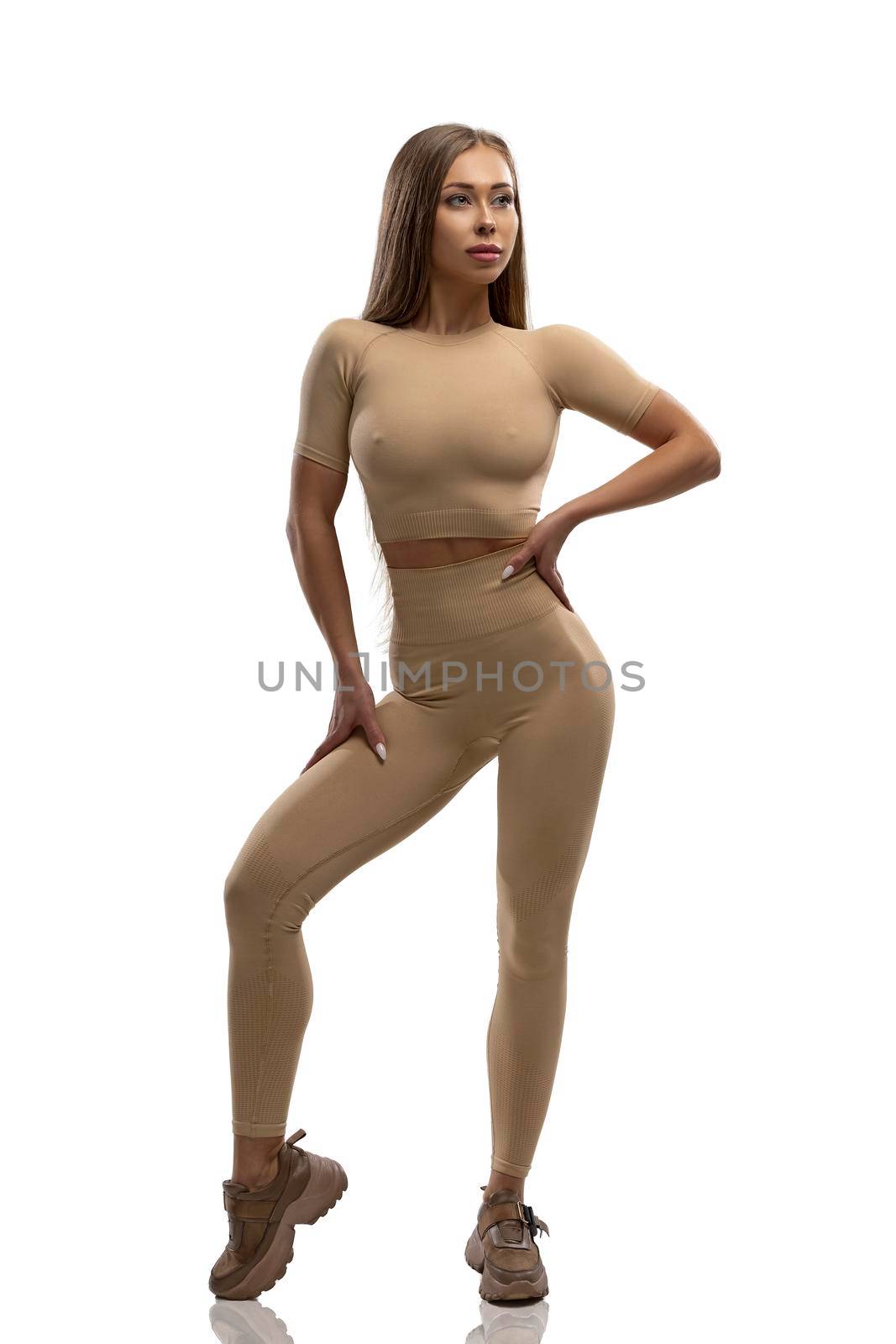 Photo of a muscular woman in beige sportswear on a white background. Health, beauty and motivation.